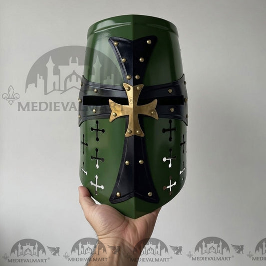 Green and black medieval helmet with gold cross held by a hand against a gray background.